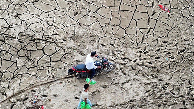 Motorbike and man carrying water cans walking on dry, cracked soil